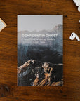 Book titled 'Confident in Christ' on a wooden surface with earbuds and a box.