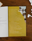 Open book with a yellow table of contents page on a wooden surface with wireless earbuds.