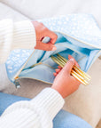 Person holding gold straws in a light blue pouch on a beige couch.