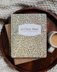 Notebook titled 'In Christ Alone' on a wooden tray with a cup of coffee