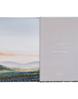 Open book with landscape illustration on one page and gray textured cover on the other