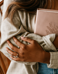 Person holding a pink Bible with floral design, wrapped in a beige blanket.
