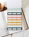 Sheet of colorful planner stickers on an open book with a cup of coffee.