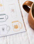 Designs of mugs on a paper sheet with a brown mug containing a dark liquid.