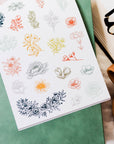 Sheet of floral stickers on a green surface with a cup and glasses in the background