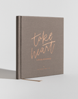 Brown book titled 'take heart' with rose gold text on a light gray background