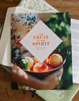 Book titled 'The Fruit of the Spirit' on a wooden surface with a floral patterned book.