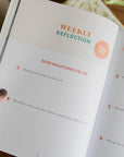 Open book with 'Weekly Reflection' section on a wooden surface