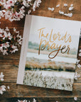 Book titled 'The Lord's Prayer' on a wooden surface with cherry blossoms