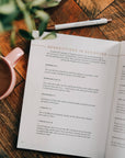 Open book on a wooden table with a pen and mug nearby