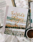Book titled 'The Lord's Prayer' on a table with a cup of coffee and other items.