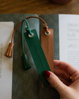 Hand holding a green leather bookmark with tassel on an open book