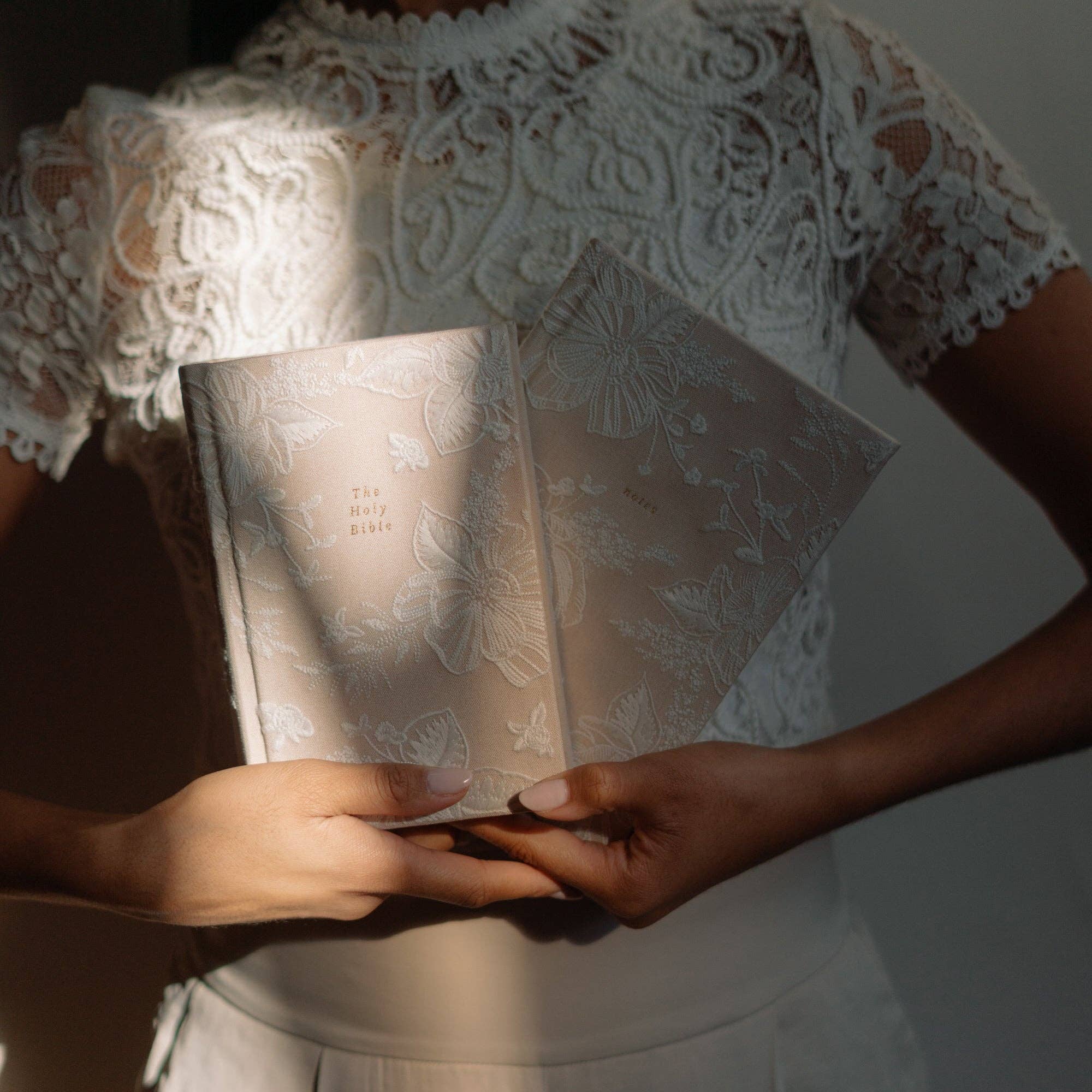 Person holding two patterned books with a lace garment in the background
