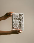 Person holding a textured rectangular object against a plain background