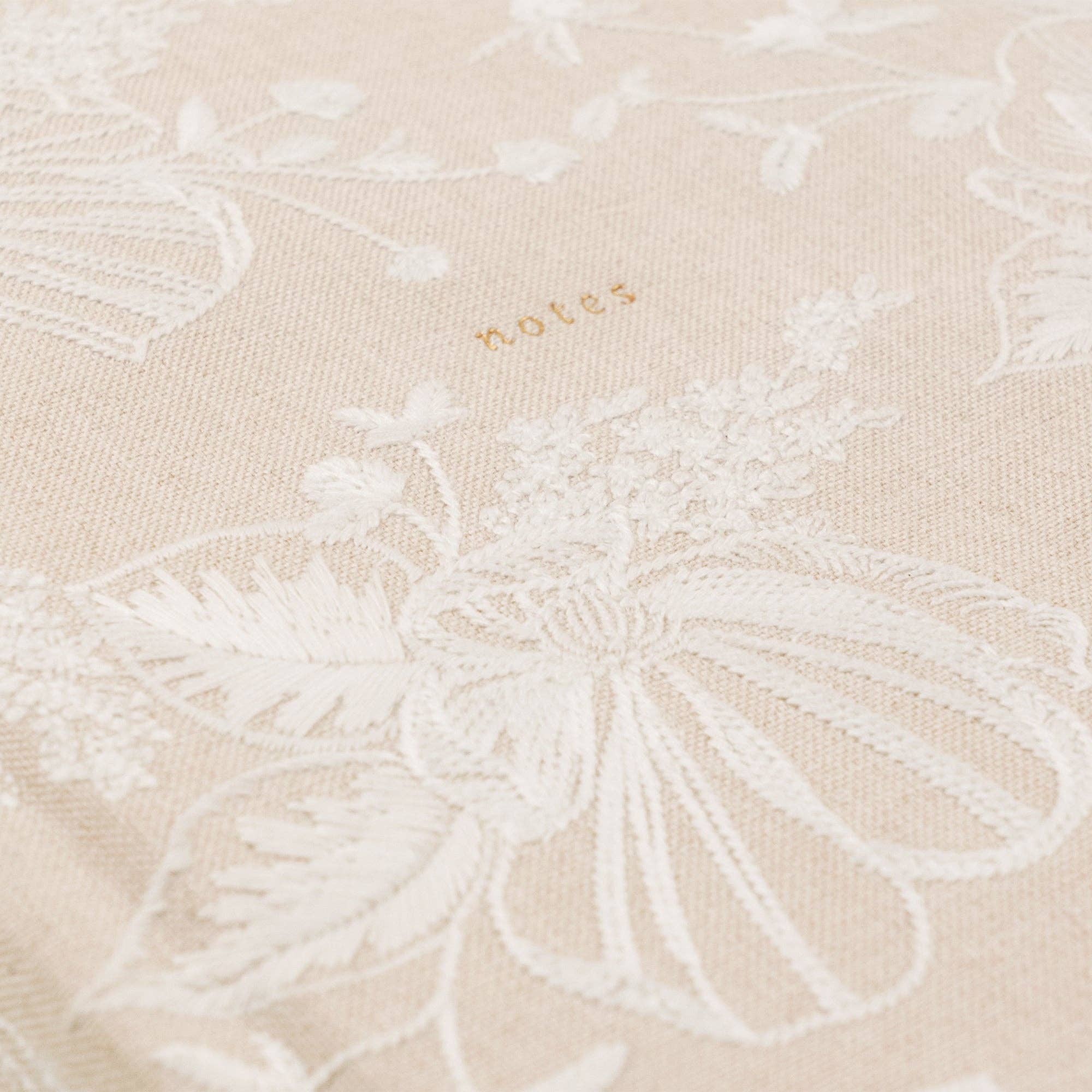 Beige fabric with white floral embroidery and 'notes' text.