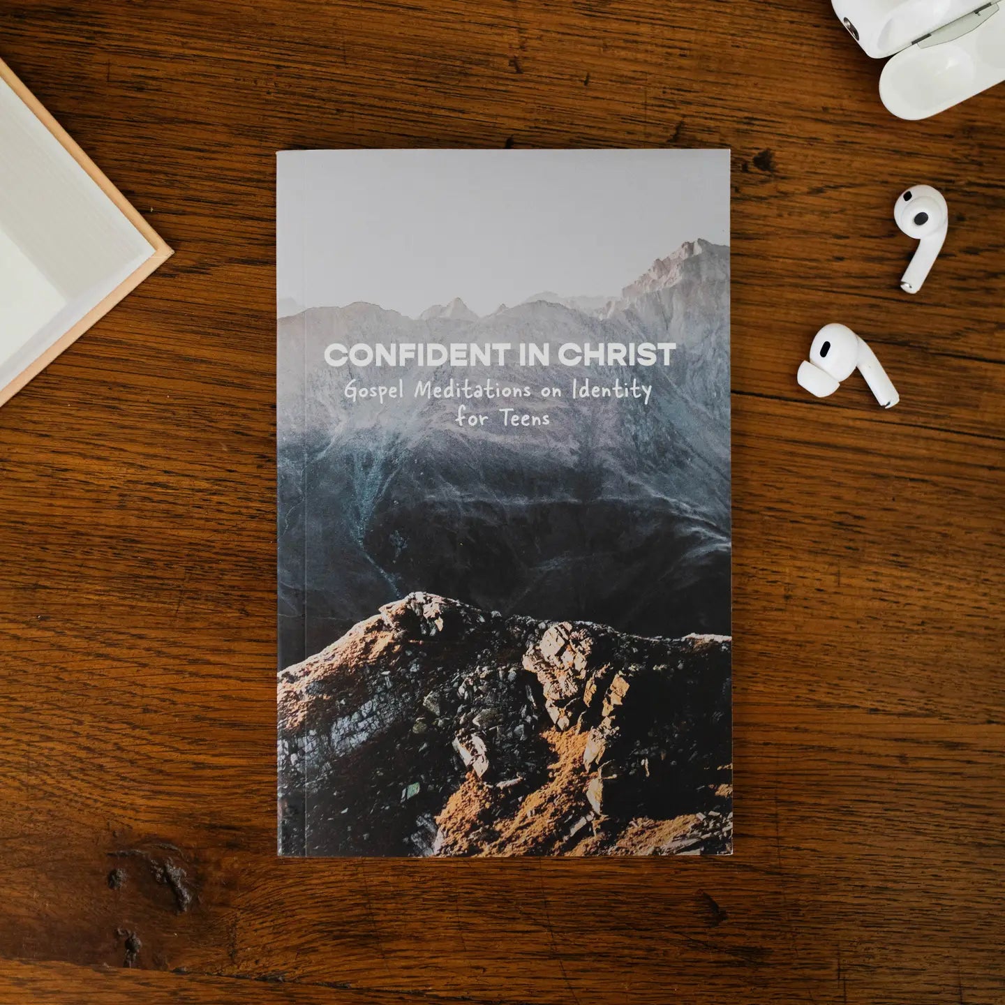 Book titled 'Confident in Christ' on a wooden surface with earbuds and a box.