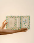 Hand holding an open book with decorative pages on a beige background