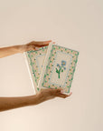Two hands holding two notebooks with floral designs on a beige background