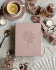 Pink notebook with floral design on a decorative table with tea and candles