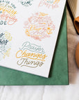 Notebook with inspirational quotes on a green surface next to a cup of coffee.