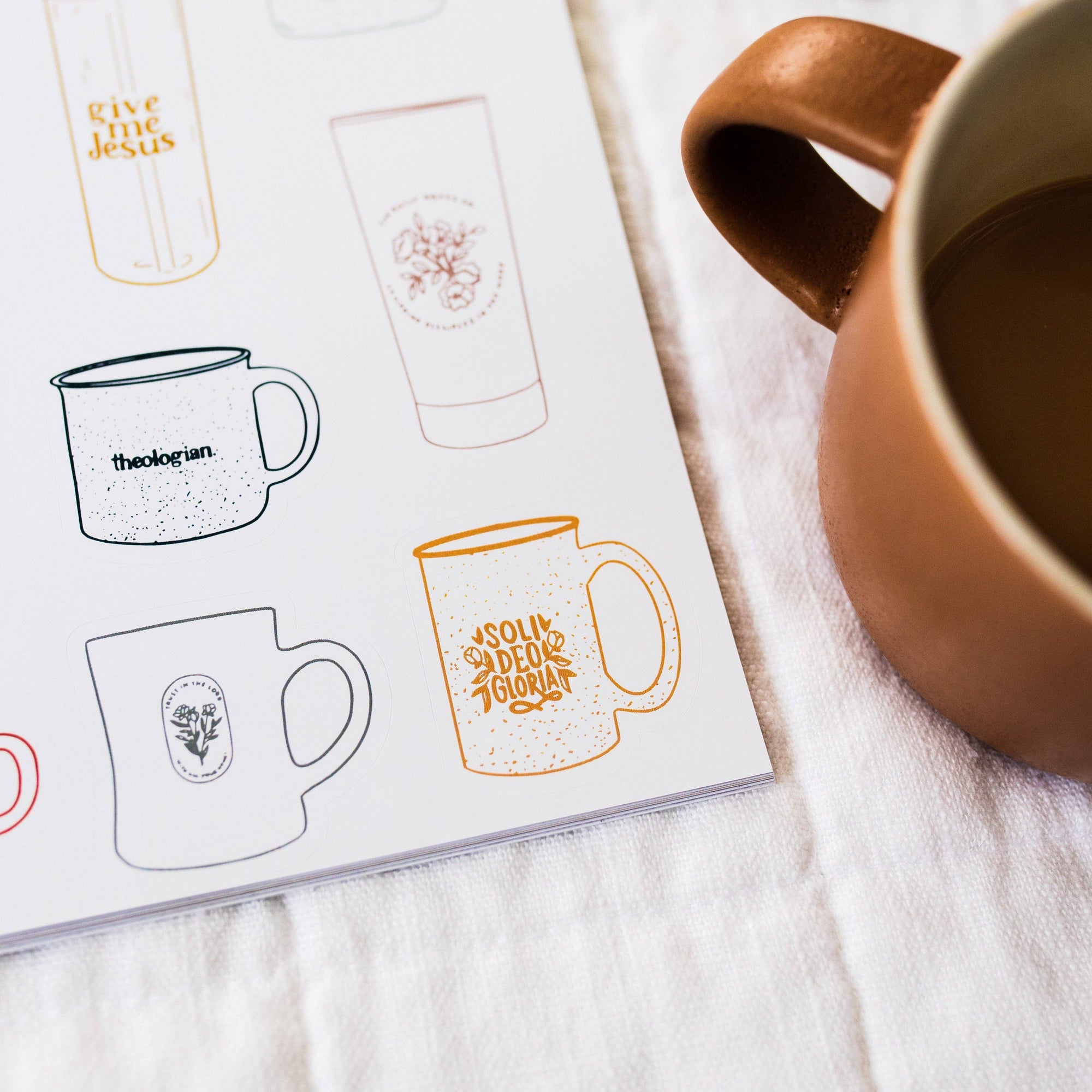 Designs of mugs on a paper sheet with a brown mug containing a dark liquid.