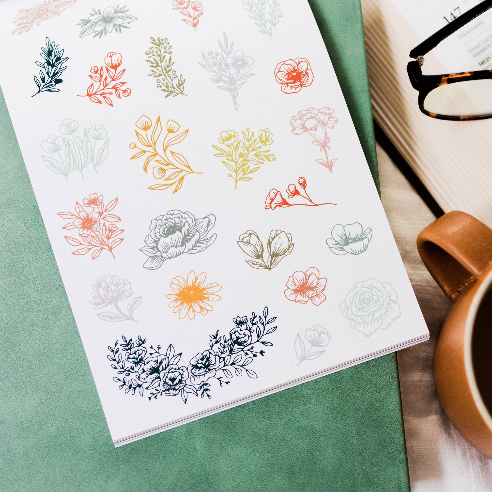 Sheet of floral stickers on a green surface with a cup and glasses in the background