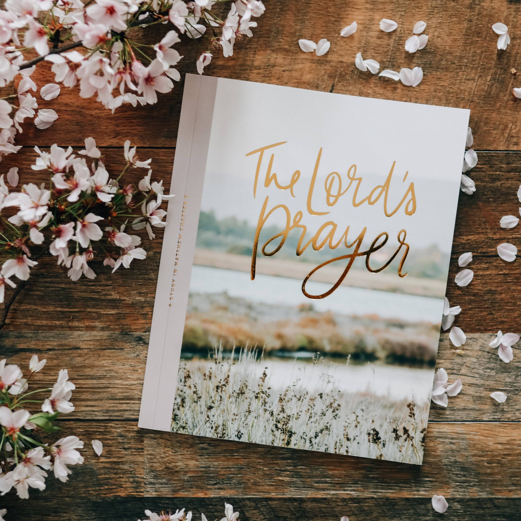 Book titled 'The Lord's Prayer' on a wooden surface with cherry blossoms