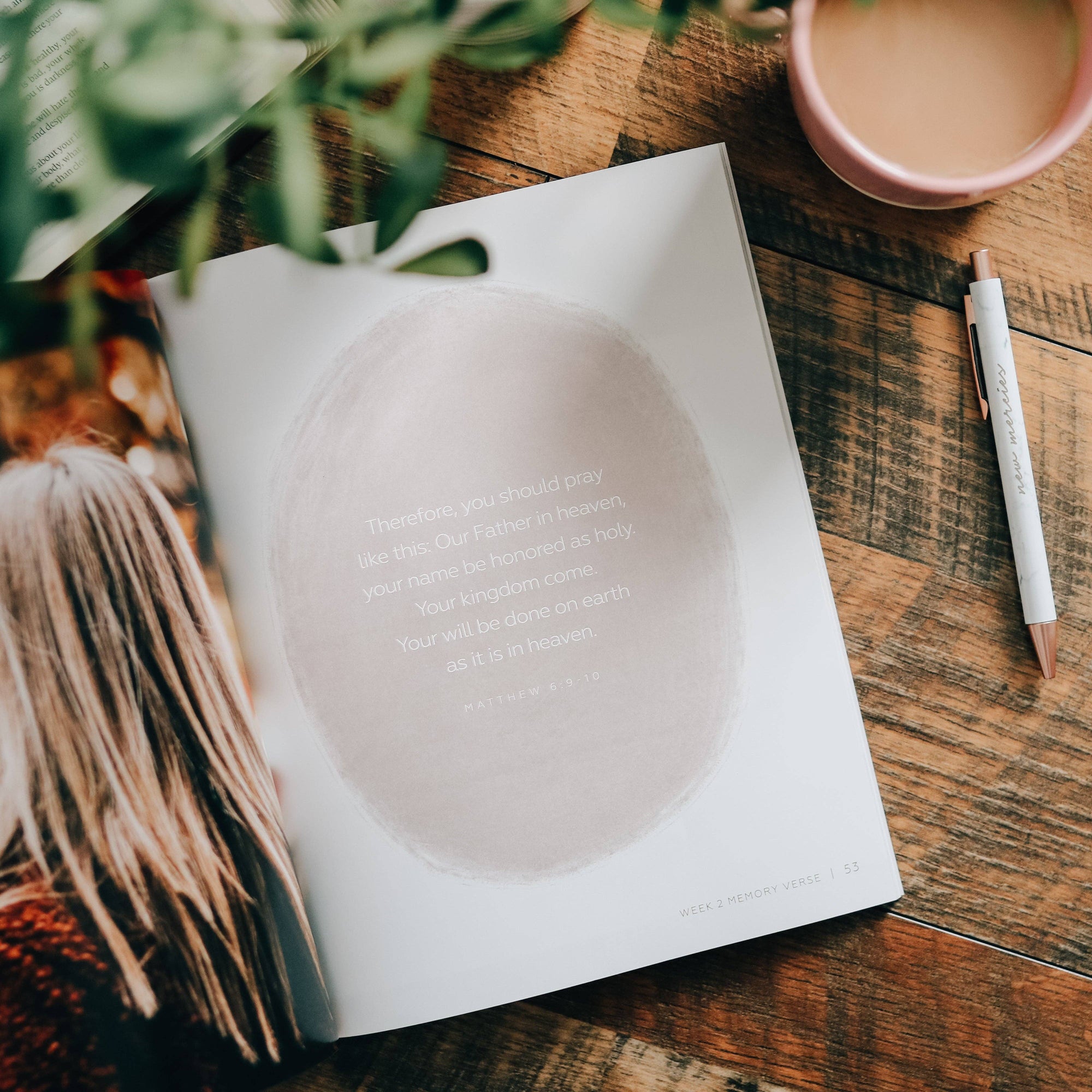 Open book on a wooden table with a pen and plant