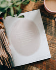 Open book on a wooden table with a pen and plant