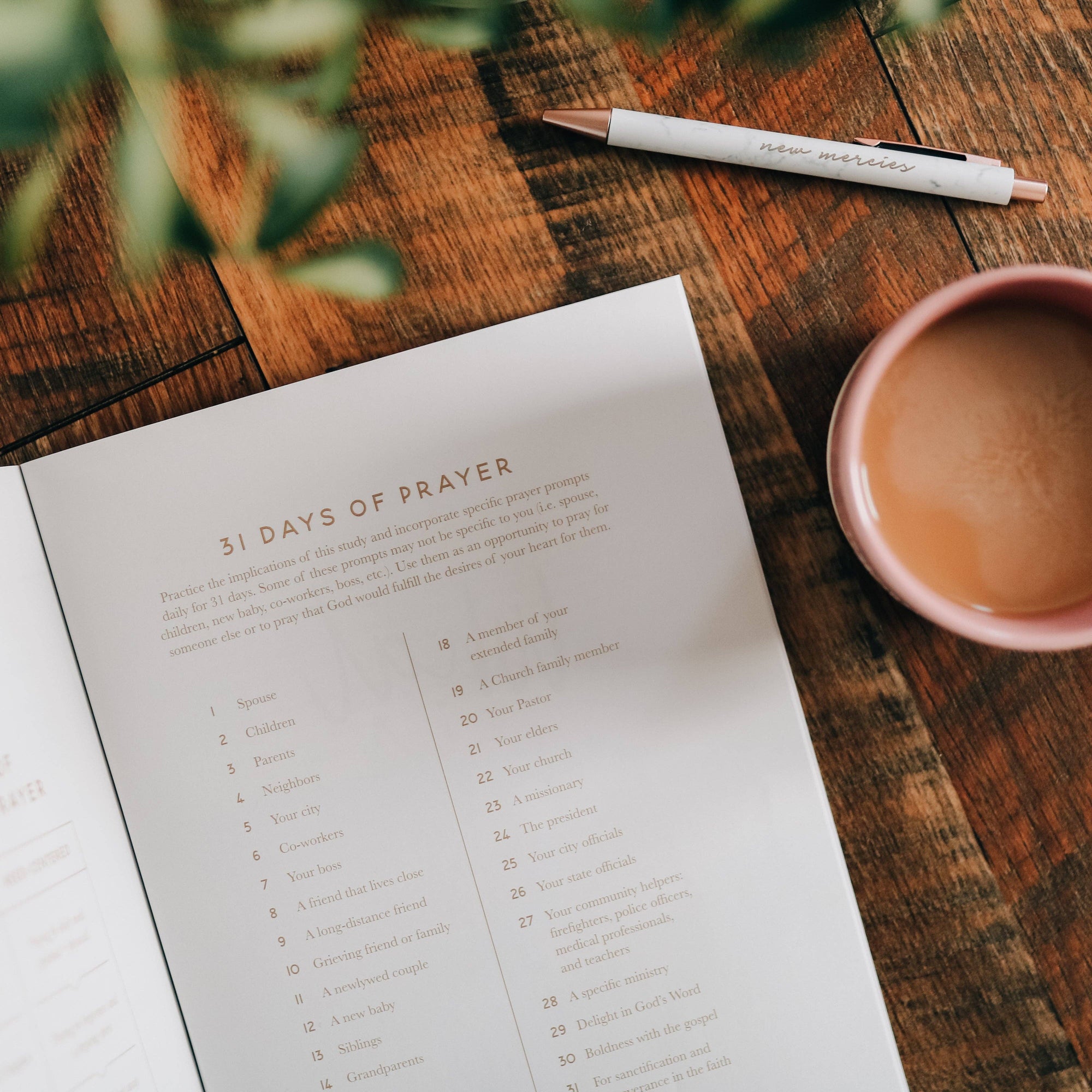 Sheet of paper titled &#39;31 Days of Prayer&#39; on a wooden table with a pen and cup of coffee.