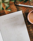 Sheet of paper titled '31 Days of Prayer' on a wooden table with a pen and cup of coffee.