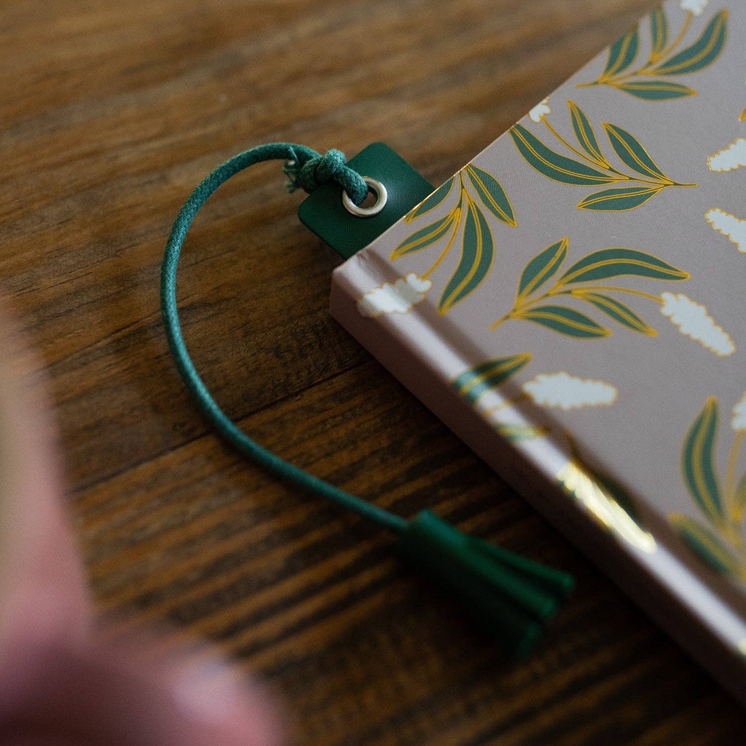 Green cord bookmark on a notebook with leaf pattern on a wooden surface