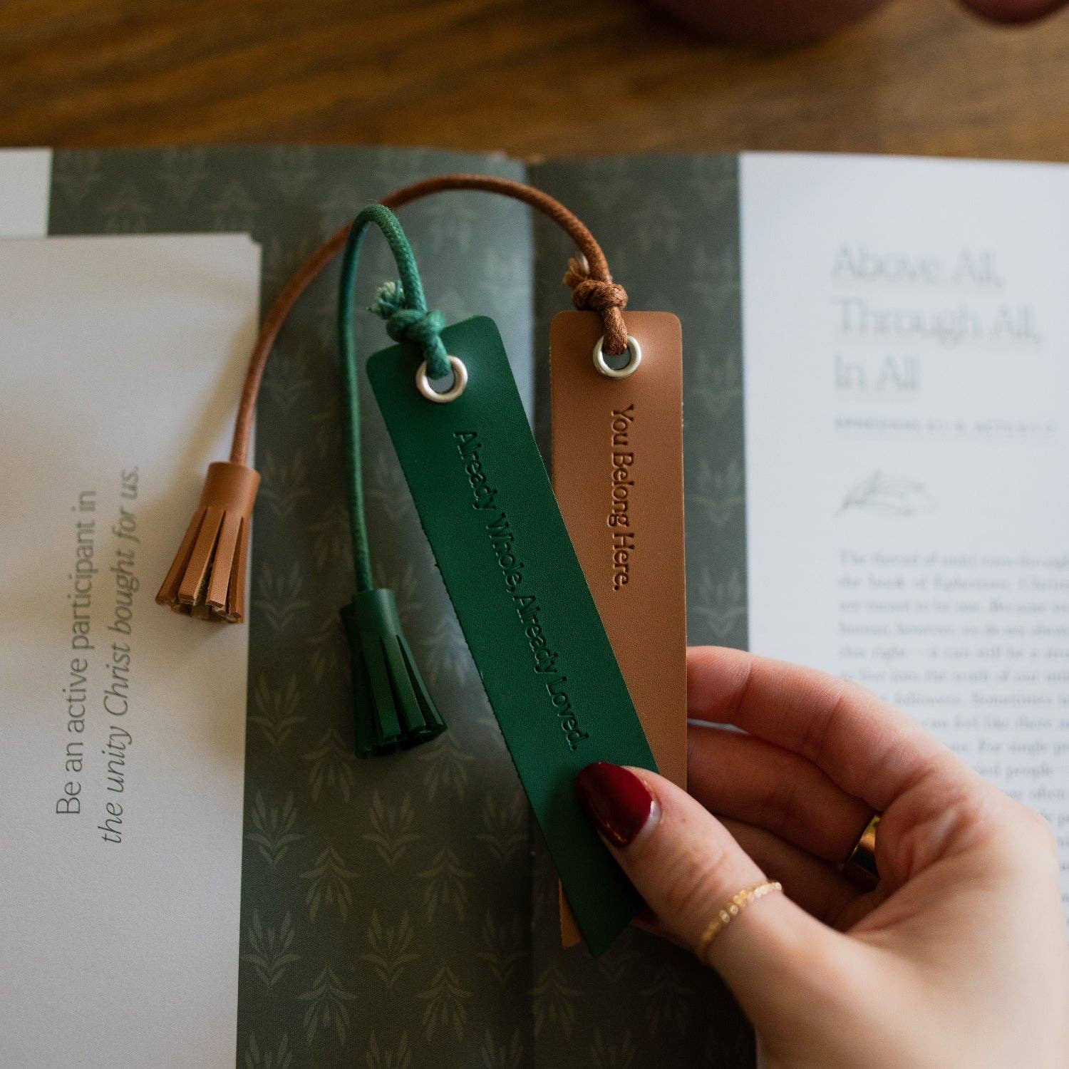 Hand holding a green leather bookmark with tassel on an open book